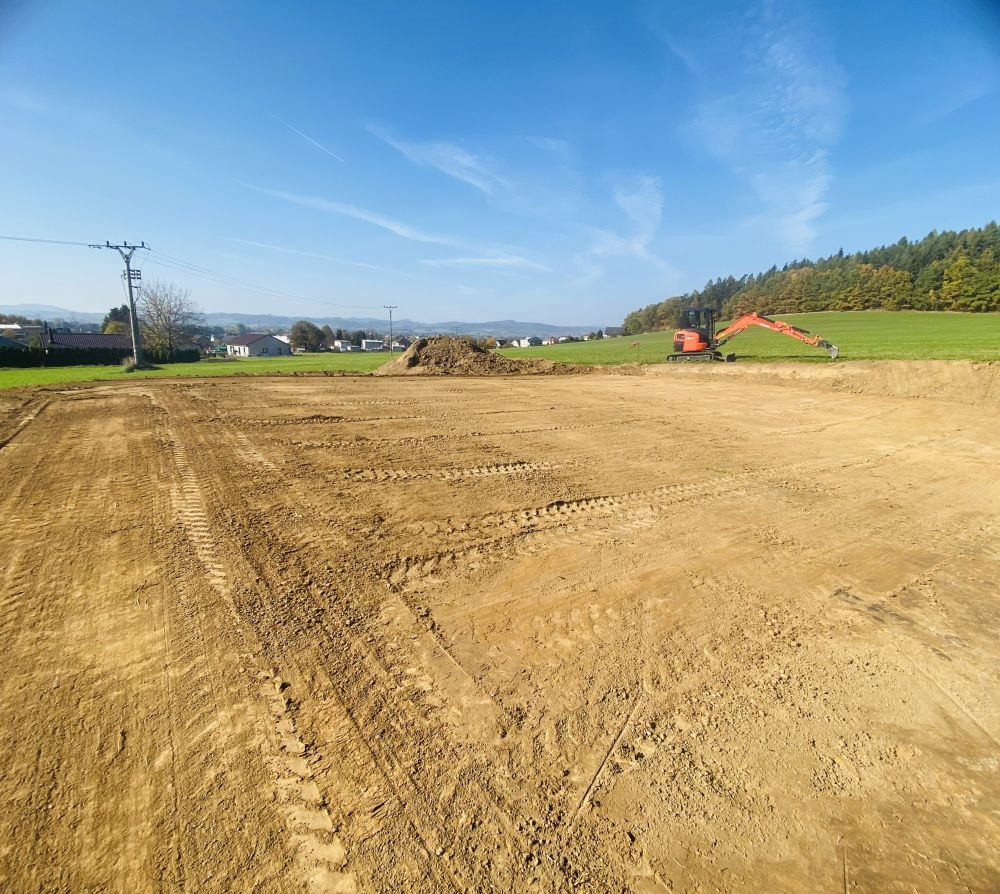 Rozlehlá srovnaná parcela připravená ke stavbě, v pozadí vesnice