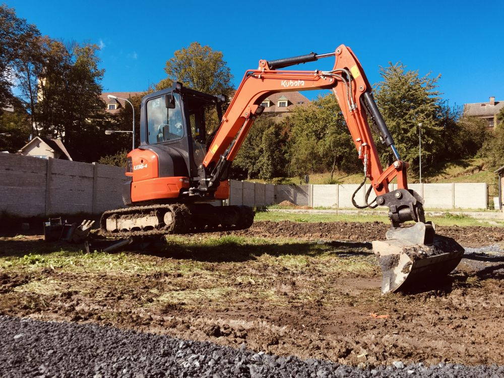 Srovnávání terénu na&nbsp;pozemku mezi betonovým plotem a&nbsp;zástavbou